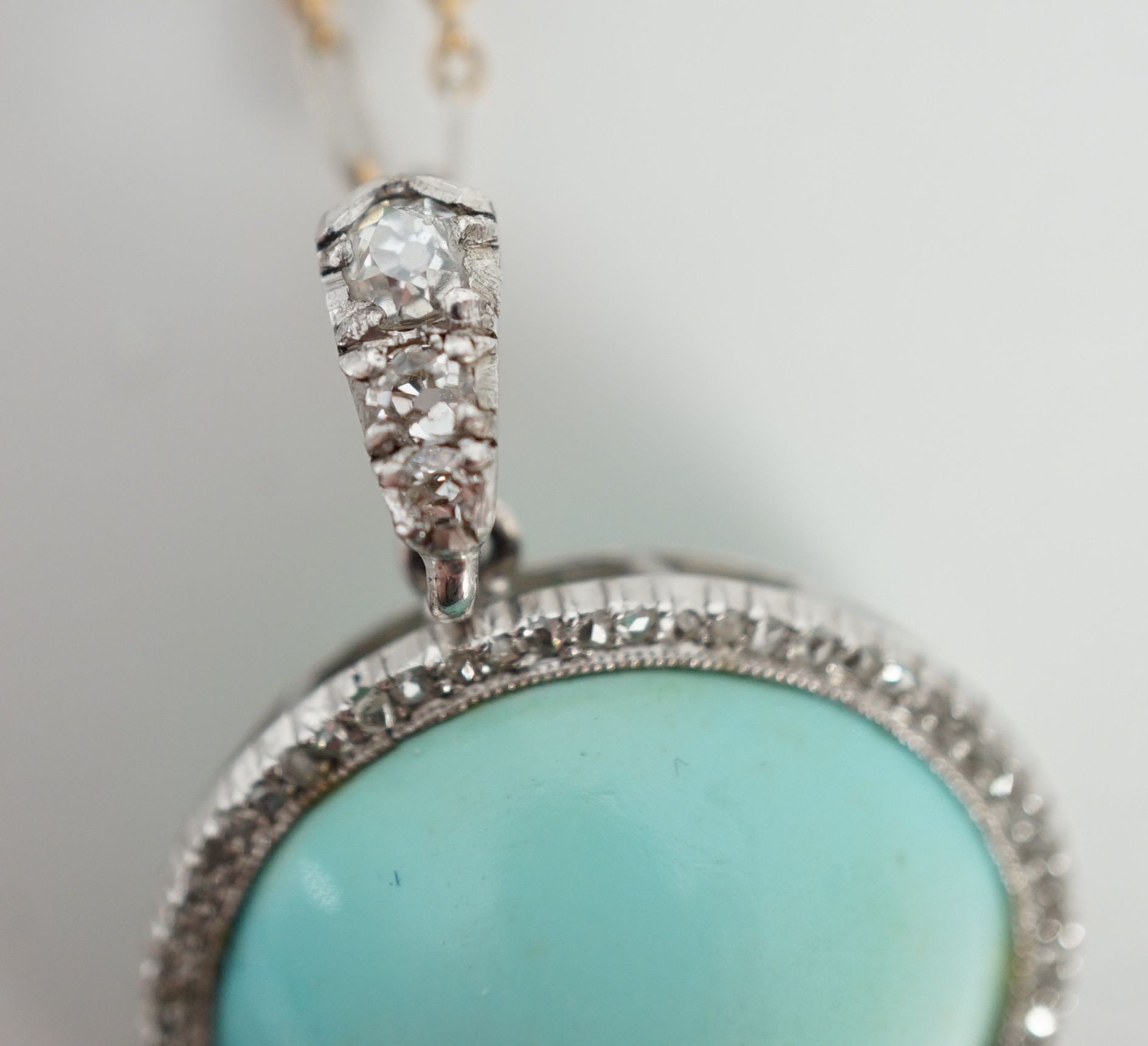 An early 20th century platinum and turquoise set pendant, with diamond chip border and diamond set bale, on a 15ct two colour gold fine link chain